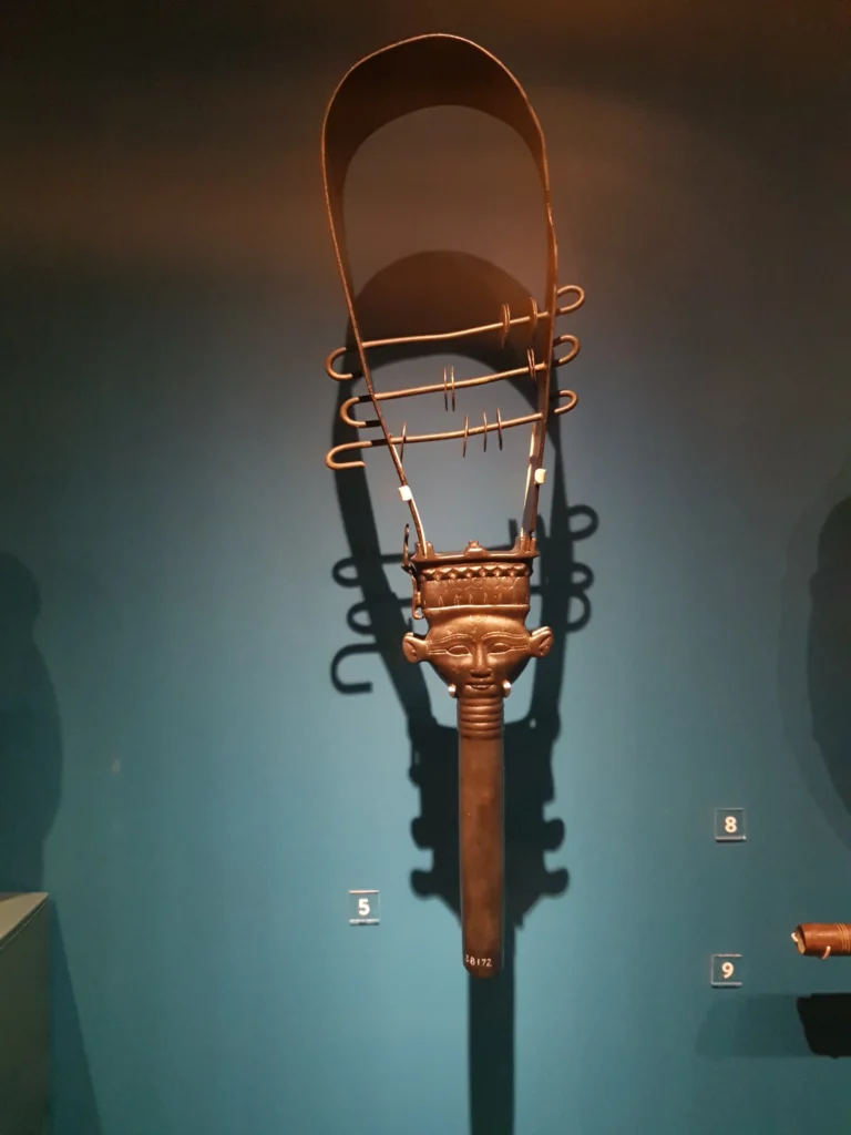 Sistro egipcio antiguo iluminado en exhibición de museo.