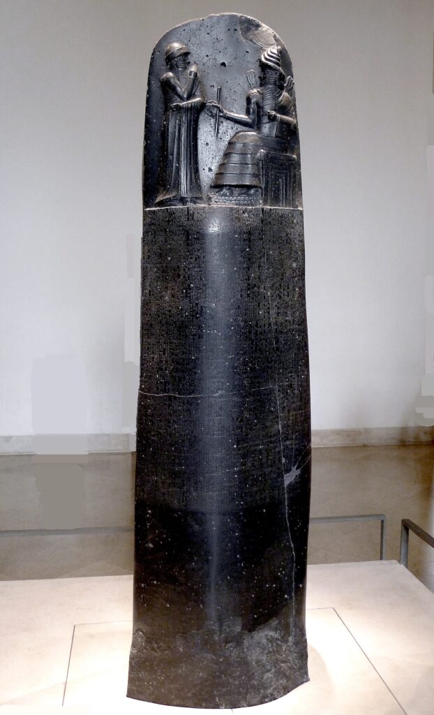 Estela tallada en piedra con escritura cuneiforme: el rey Hammurabi recibe instrucciones del dios Shamash en la parte superior. Debajo se encuentra inscrito su código legal.